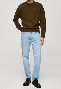 Brauner Strickpullover mit Rundhalsausschnitt, kombiniert mit hellblauen geraden Jeans. Schwarze Lederschuhe ergänzen das Outfit.