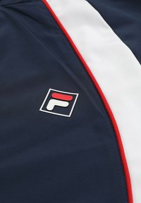 Laivastonsininen kangas, jossa valkoisia ja punaisia raitoja, sekä pieni neliönmuotoinen logo, jossa on puna-valkoisia kuvioita.