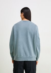 Sweater in vervaagde lichtblauwe kleur, gemaakt van katoen, met een ronde hals, ribgebreide boorden en een relaxte pasvorm met een zachte, licht gestructureerde oppervlakte.
