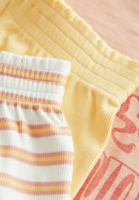 Twee elastische taillebandstukken: één effen lichtgeel met ribbelstof, en een andere witte met roze en gele strepen. Zachte textuur en rekbare stof.