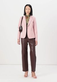 Light pink blazer over a floral-patterned top, paired with brown leather pants and nude heeled sandals. Bag has a curved design.
