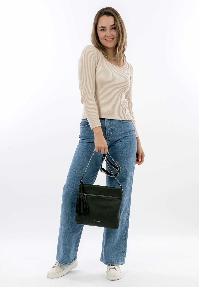 Maglione beige a coste, jeans blu a vita alta e una borsa in pelle nera con un pon-pon, tenuta sul lato destro. Sneakers bianche ai piedi.
