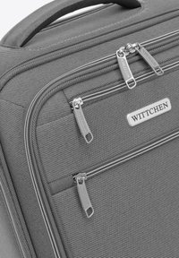 Grauer Reisekoffer von WITTCHEN mit strukturiertem Stoff, mehreren Reißverschlüssen und einem geprägten Metalllogo. Kompakt im Design mit robustem Griff.