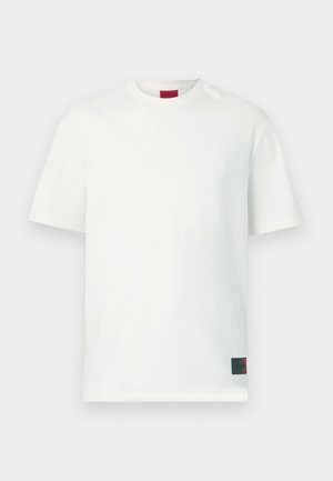 Weißes Baumwoll-T-Shirt mit rundem Halsausschnitt, kurzen Ärmeln und einem roten Logoetikett an der unteren linken Seite. Glatte Textur, Standardpassform.