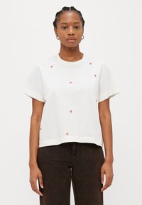 T-shirt bianca in cotone con maniche corte e taglio dritto, caratterizzata da piccoli motivi ricamati a forma di fragola sparsi sul tessuto.