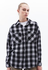 Svart och grå rutigt flanellskjorta med knappstängning fram, två bröstfickor och klassisk krage. Mjuk textur, avslappnad passform, långa ärmar.