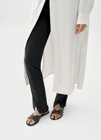 Chemise blanche boutonnée avec une finition texturée, associée à un pantalon noir ajusté et des sandales noires à lanières croisées et semelles plates.