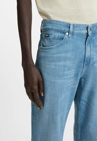 Jeans in denim blu chiaro con taglio dritto, dotati di un'etichetta nera del marchio, design classico a cinque tasche e una leggera scoloritura sul tessuto.