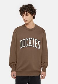 Felpa marrone con scollo rotondo e maniche lunghe. Presenta la scritta ricamata bianca "DICKIES" sulla parte anteriore. Tessuto morbido e di texture.