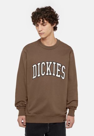 Sudadera marrón con cuello redondo y mangas largas. Presenta el texto bordado en blanco "DICKIES" en la parte frontal. Tejido suave y texturizado.