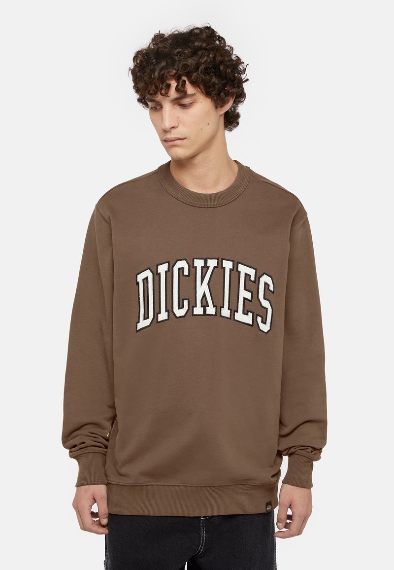 Felpa marrone con scollo rotondo e maniche lunghe. Presenta la scritta ricamata bianca "DICKIES" sulla parte anteriore. Tessuto morbido e di texture.