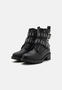 Black ankle boots made of textured leather, featuring silver hardware, two wide straps adorned with eyelets, and a chunky heel.