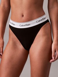 Juoda medvilninė bikinių kelnaitės su balta elastinga juosta, kurioje yra "Calvin Klein" logotipas. Dizainas apima minimalistinį tanga stilių.