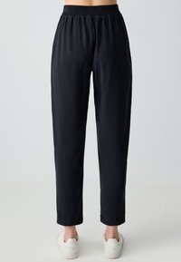 Pantalons noirs, légers, fuselés avec une taille élastique. Texture lisse, longueur cheville, associés à des baskets blanches.