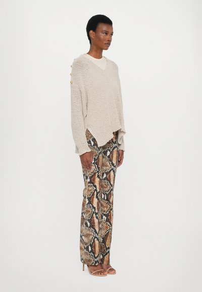 Beige knitted sweater with V-neck and side button accents, paired with brown snake-print pants. Model wearing nude heeled sandals.