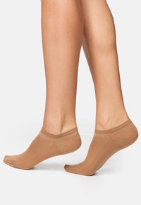 Calzini alla caviglia color nudo con una texture liscia, design a taglio basso e un motivo ondulato di cuciture bianche lungo il bordo.