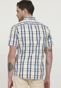 Chemise à manches courtes à carreaux crème, bleu et marine, dotée d'un col boutonné et d'un tissu en coton texturé. La vue arrière montre les coutures des épaules.