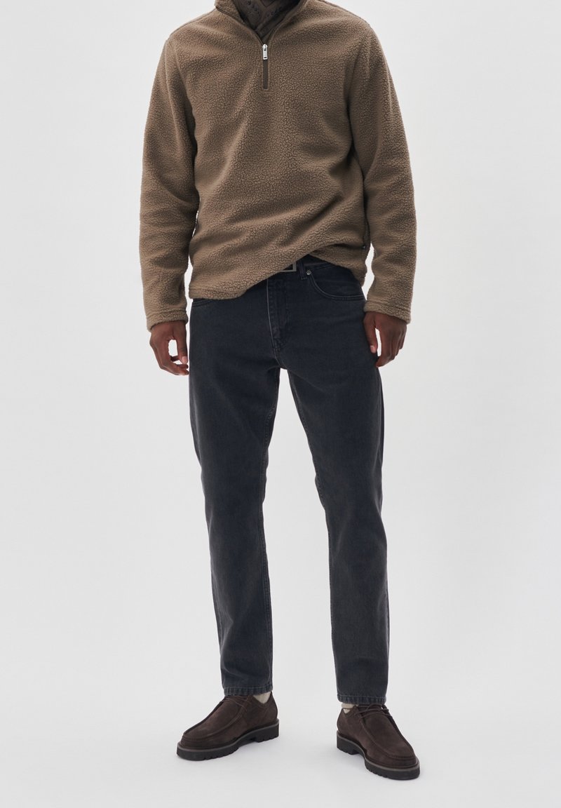 Pullover in pile beige con zip a tre quarti, jeans in denim scuro, scarpe in suede marrone scuro, vestibilità slim, tessuto testurizzato, design semplice.