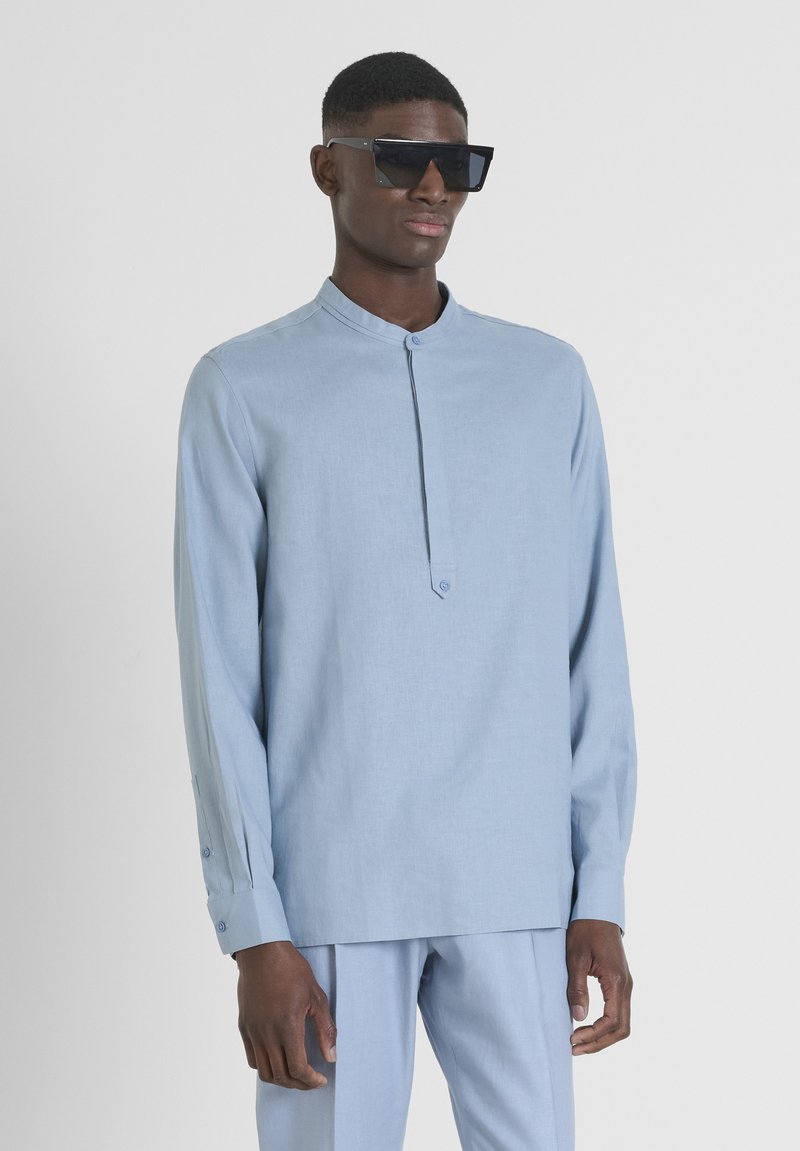 Camicia a maniche lunghe azzurro chiaro con colletto alla cinese, patta frontale con bottone e polsini con dettagli a bottone. Tessuto morbido e strutturato.