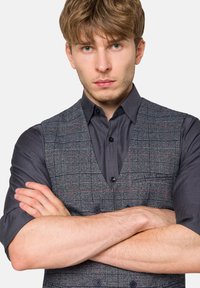 Szary kamizelka w wzory o zorganizowanym kroju na ciemnej koszuli. Posiada dekolt w serek, zapięcia na guziki oraz subtelny czerwony kratkowany wzór.