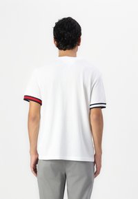 Hvid kortærmet t-shirt med kontrasterende marineblå og røde striber ved ærmerne. Blødt stof, afslappet pasform, rund halsudskæring og flad kant.