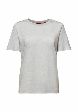 Osoba ubrana w błyszczącą niebieską puchową kurtkę, jasnoszary top, metaliczną ciemnoszarą spódnicę z szerokim paskiem, beżowe skarpetki i beżowe buty trekkingowe, stojąca z rozstawionymi nogami.