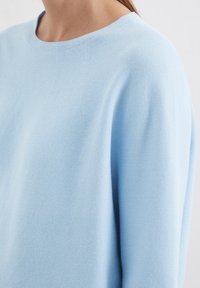 Pull en tricot bleu clair avec un col rond et un tissu texturé, présentant une coupe décontractée et des détails côtelés subtils.