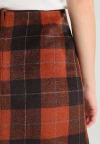 Gonna a quadri di lana arancione, nera e grigia. Presenta un design aderente con una cerniera visibile sul retro e una superficie texture.