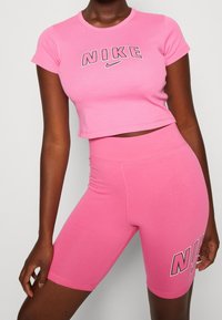 Rosa kortärmad t-shirt och matchande högmidjade shorts, med Nike-logotypen i en kontrasterande stil på framsidan av shortsen. Mjukt tyg.