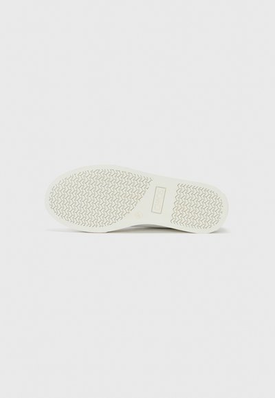 White rubber sneaker sole featuring a textured, zigzag pattern for traction. The upper edge is slightly rounded, labeled with the brand name.