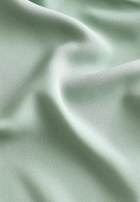 Tissu vert clair avec une surface lisse et légèrement texturée, affichant de doux plis et drapés, adapté à diverses applications textiles.