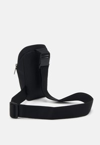 Černá crossbody taška vyrobená z měkkého materiálu. Obsahuje zipové zapínání, nastavitelný popruh a minimalistický design bez výrazných kovových doplňků nebo vzorů.