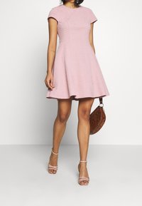 Różowa sukienka o fakturowanej powierzchni z krótkimi rękawami i rozkloszowanym dołem. W połączeniu z brązową torebką w wzory oraz jasnoróżowymi sandałkami na cienkich obcasach.