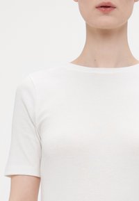 Camiseta blanca de manga corta con cuello redondo, fabricada con un tejido suave de textura con un sutil patrón acanalado, sin logotipos ni gráficos visibles.