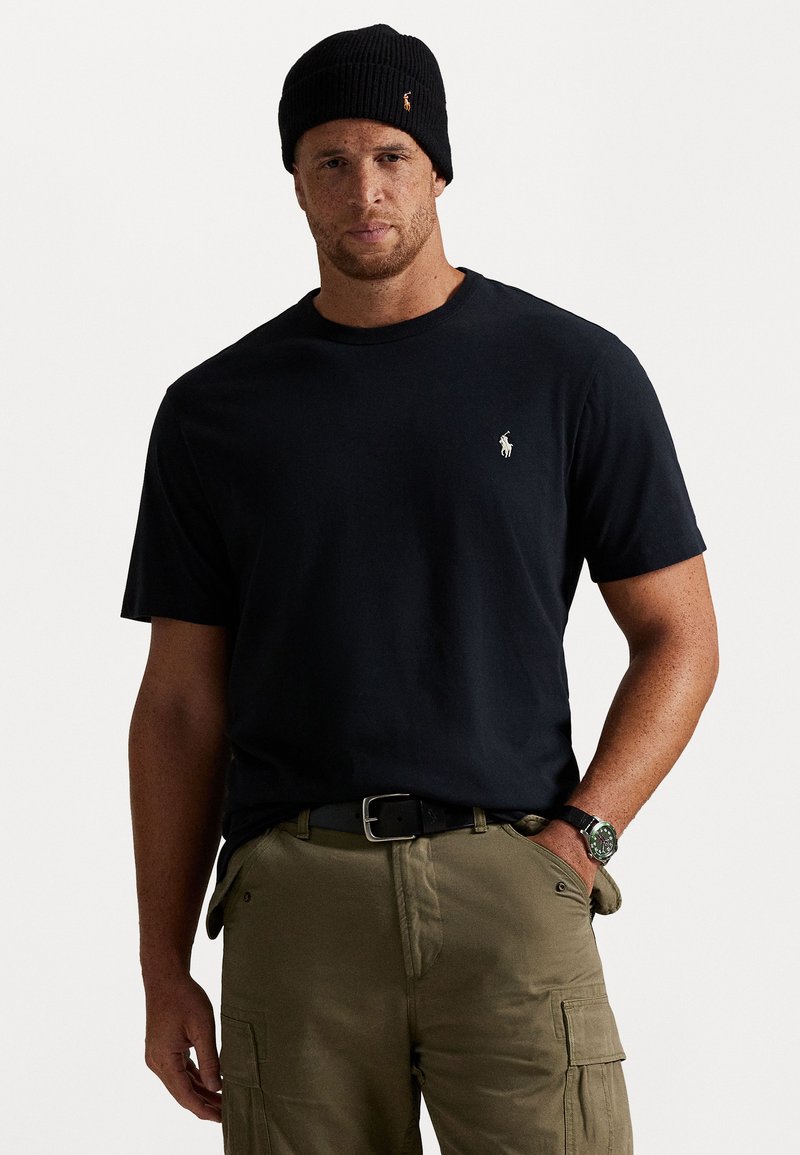 Melna kokvilnas T-krekls ar īsām piedurknēm, ar mazu izšuvumu logotipu. Valkāts ar olīvkrāsas kravas biksēm un melnu ribotu beanie cepuri.