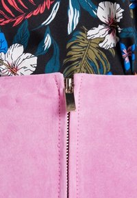 Tissu en daim rose à texture lisse, avec une fermeture éclair argentée et un motif floral en noir, bleu et vert en haut.