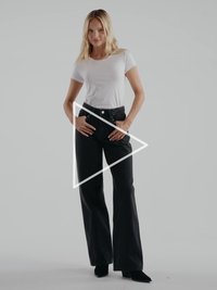 Camiseta blanca de manga corta combinada con jeans negros de cintura alta y pierna ancha. La modelo posa con las manos en las caderas frente a un fondo neutro.