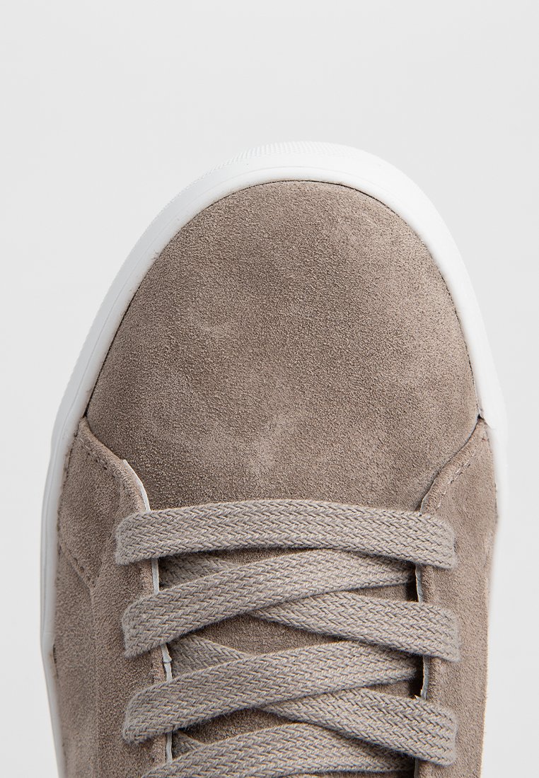 Graue Wildleder-Sneaker mit weißer Gummisohle, flachen Schnürsenkeln und einer glatten Zehenkappe. Minimalistisches Design ohne zusätzliche Akzente.