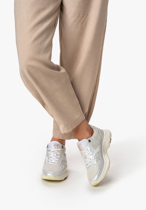 Witte sportieve sneakers met zilverkleurige accenten, bovenwerk van mesh en synthetisch materiaal, dikke zool en vetersluiting, gecombineerd met beige ontspannen pasvorm broek.