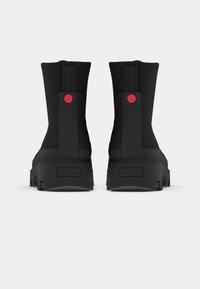 Bottes de cheville noires imperméables avec un extérieur en caoutchouc lisse, bout arrondi et un bouton rouge proéminent à l'arrière. Semelle robuste.