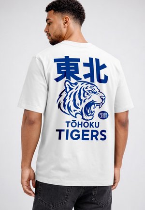 Mann trägt ein weißes T-Shirt mit blauem japanischem Text, einer Grafik eines brüllenden Tigers und dem Aufdruck „Tōhoku Tigers“ auf dem Rücken.