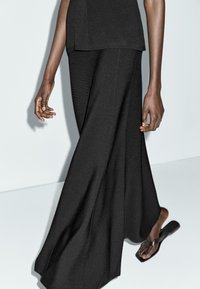 Pantaloni neri a gamba larga realizzati in un tessuto morbido, con una texture liscia e linee pulite. Indossati con una maglietta nera e calzature minimal.