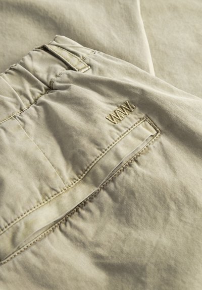 Világos bézs szövet, hímzett zsebbel és derékpánttal, a zseb fölött "WWN" hímzéssel, alkalmi nadrágon vagy rövidnadrágon.