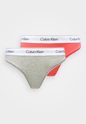 Two Calvin Klein thongs: one light gray and one coral. Both feature a white waistband with black "Calvin Klein" branding. Soft, stretchy fabric.