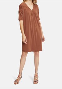 Kortärmad klänning med V-hals i brun, tillverkad av mjukt tyg med veckdetalj fram. Matchad med flerfärgade sandaletter med remmar.