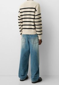 Suéter de punto a rayas en crema y negro, combinado con jeans de pierna ancha en azul claro. Textura suave, corte relajado y acabado de denim desgastado con bolsillos traseros.