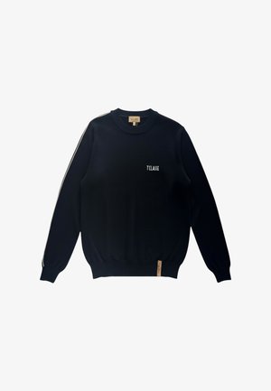 Maglione nero a maniche lunghe con scollo rotondo, strisce bianche sulle maniche, scritta "T CLASSE" sul petto e una piccola etichetta marrone chiaro vicino all'orlo.