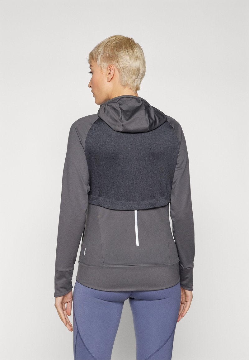 Graue Sportjacke mit einem verkürzten Rücken, Kapuze und langen Ärmeln. Aus glattem Stoff, mit Farbblockdesign und reflektierenden Akzenten.