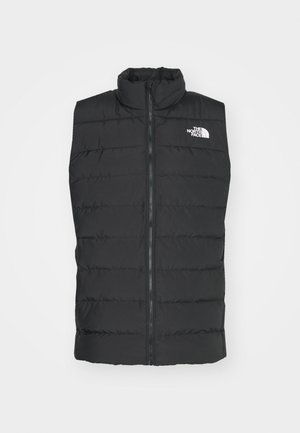 Sort polstret vest med høj krave, lynlås lukning, kviltet design og signaturlogo på brystet, der fremviser en glat, mat overflade.