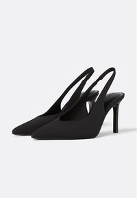 Crne slingback cipele s visokom potpeticom, špicastog vrha i izrezanim stranama. Izrađene od mekanog materijala, s tankom potpeticom i glatkim unutarnjim oblogom.